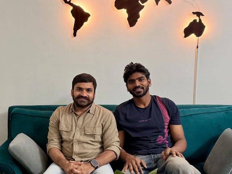 Sandeep and cricketer K S Bharat sitting together on a green sofa beneath a glowing wooden world map