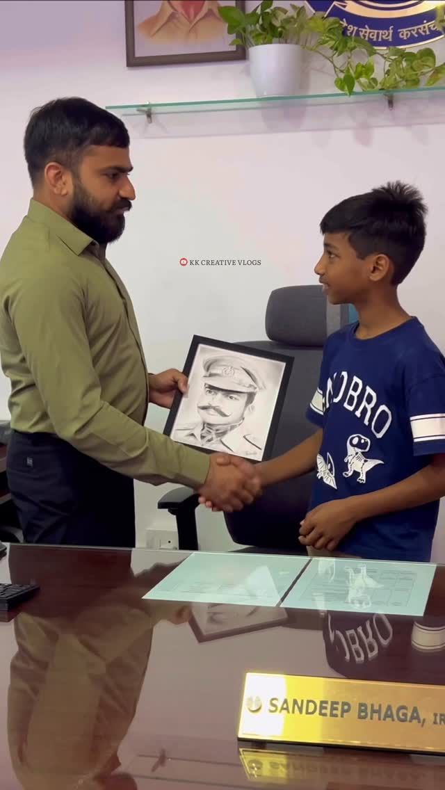 Sandeep Bhaga at his office desk shaking hands with a boy who presents him a framed pencil sketch